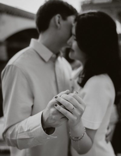 Black-and-white close-up of the couple leaning together and holding hands, with the Eiffel Tower blurred behind them.