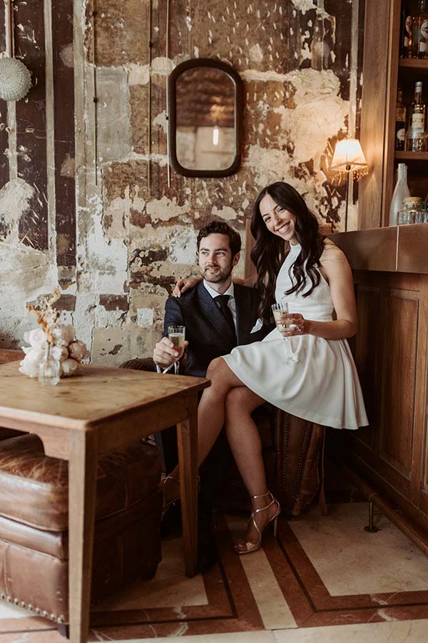 Un couple en tenue de mariage trinque avec deux verres dans un café du 11e arrondissement.